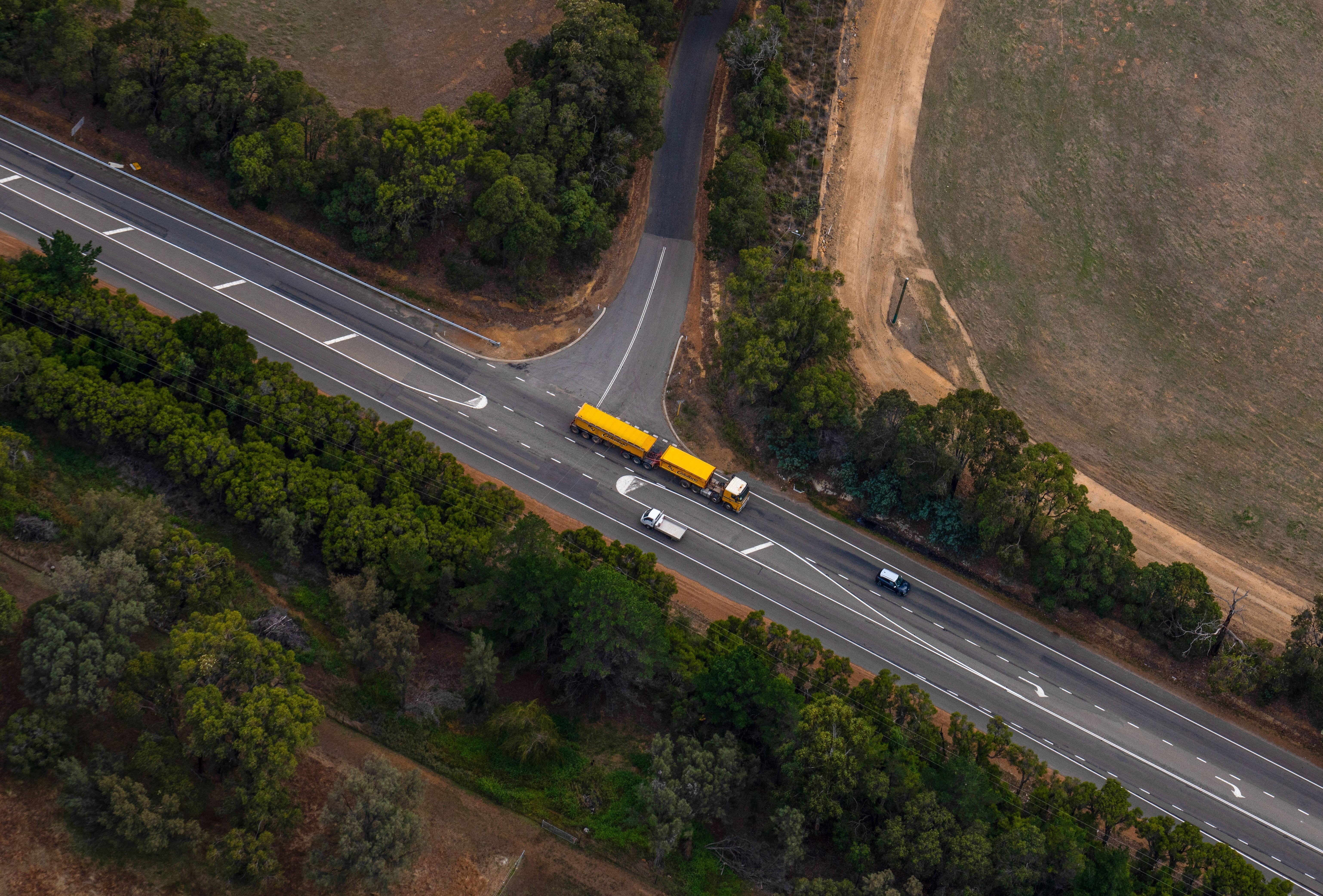 Long yellow truck pictured driving along road from above