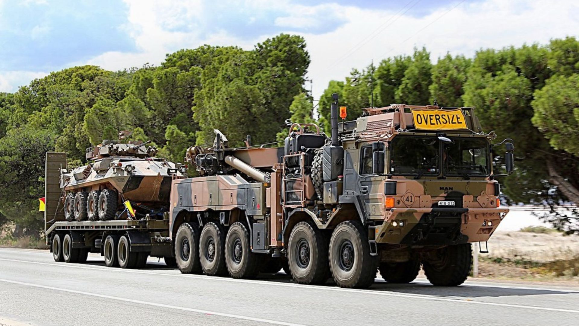 Australian Army Truck with trailer towing a tank driving along a road
