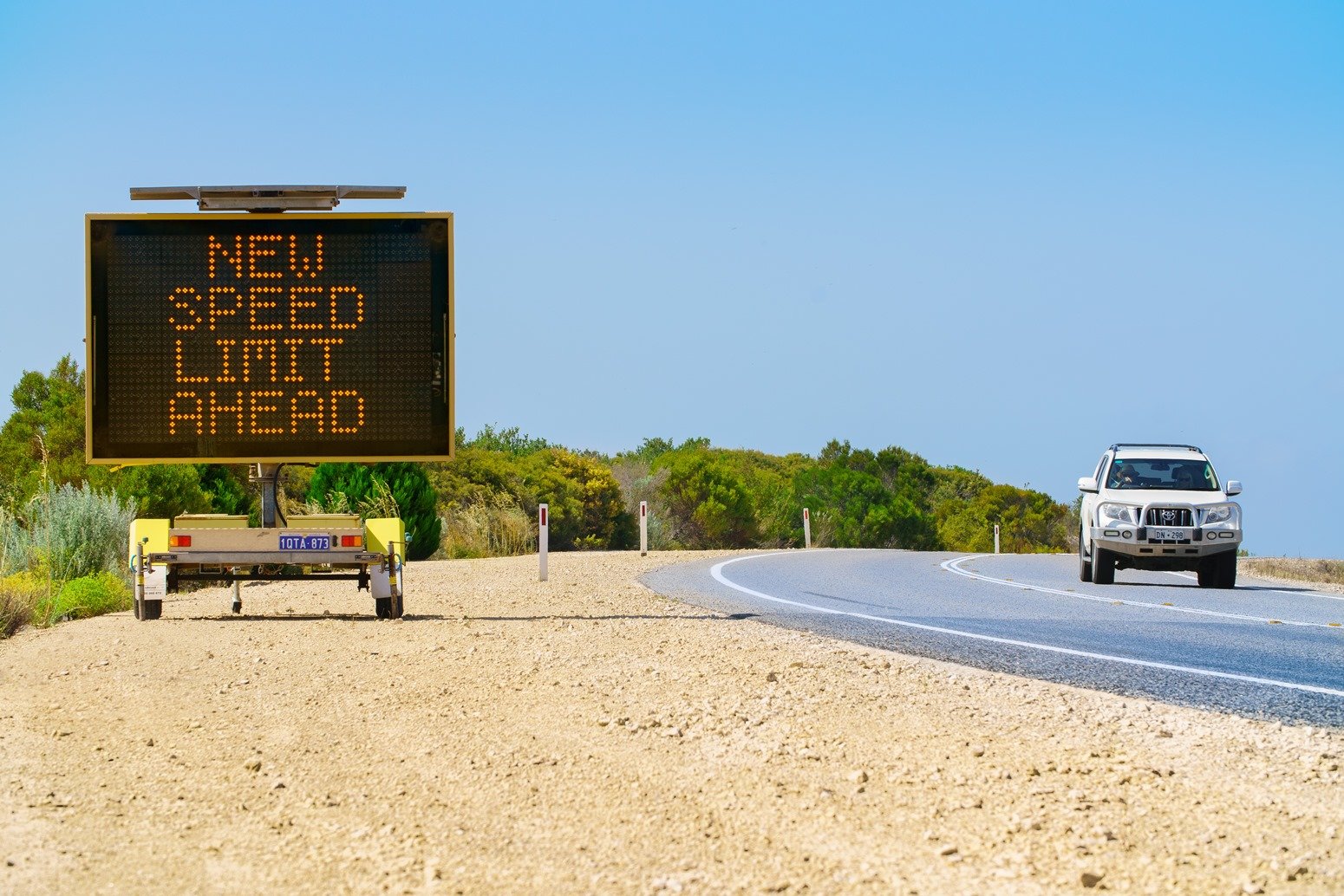 Car travelling on regional road with new speed limit ahead electronic sign